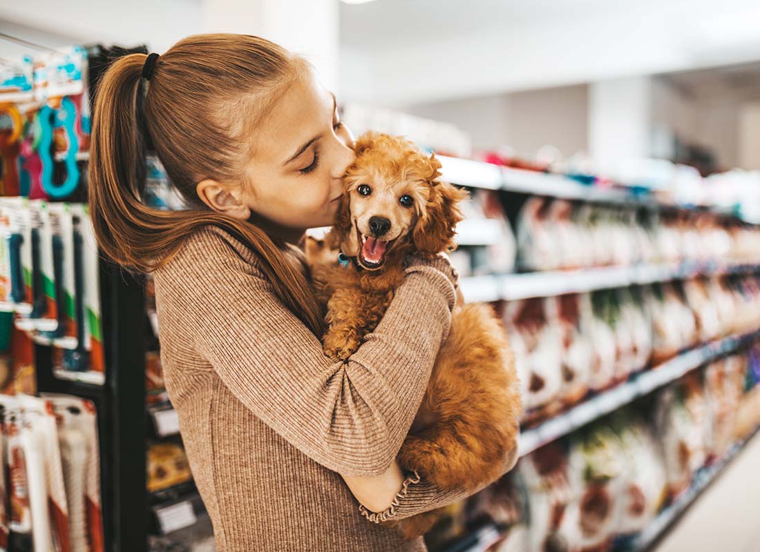 Pet Business Insurance - Young and Joyful Girl Shopping in a Pet Store with Her New Poodle Puppy and Giving Him with a Kiss