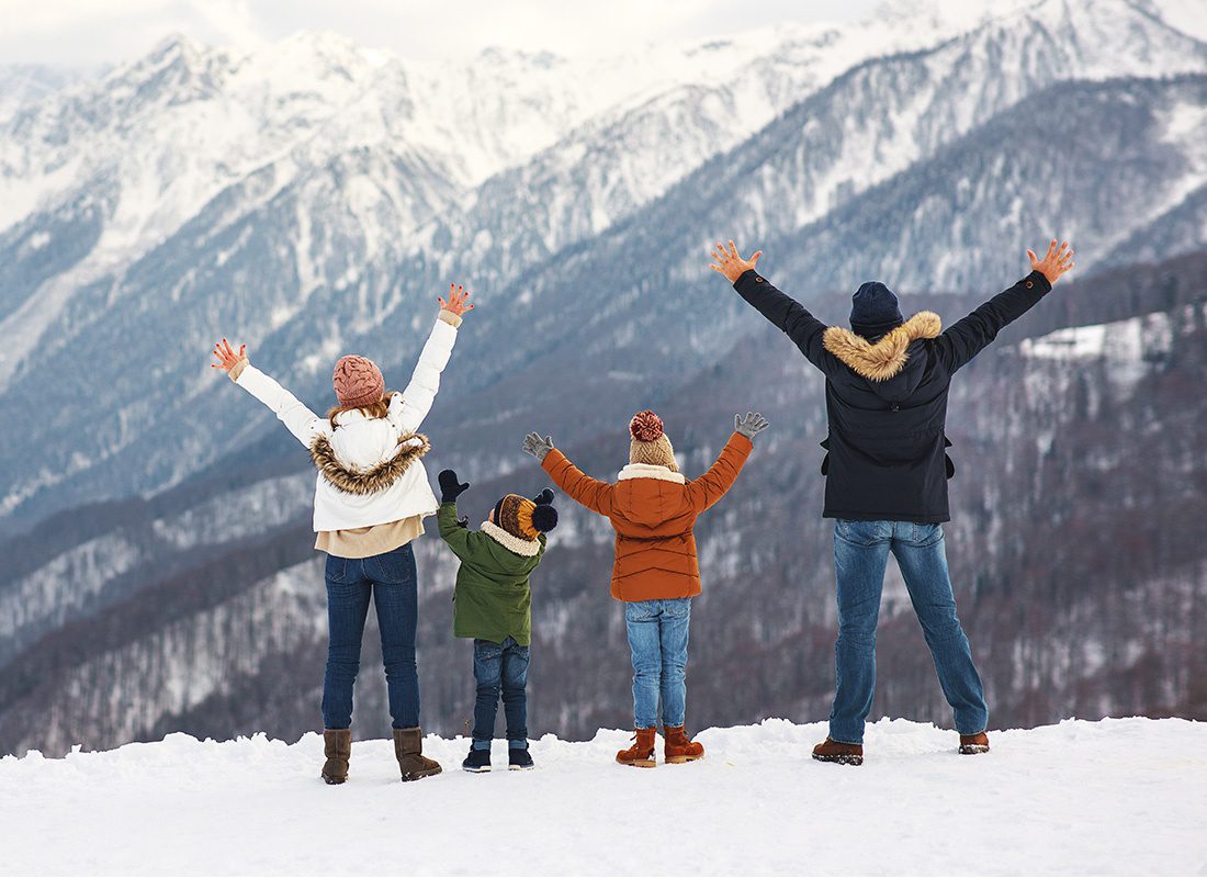 Insurance Solutions - Rear View of a Family with Two Young Kids Putting Their Hands Up in the Air as They Enjoy the Views of the Snowy Mountains During the Winter