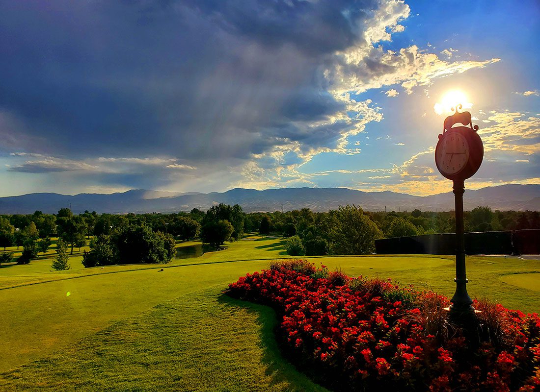 Service Center - View of a Decorative Clock on a Flower Bed with Red Flowers on a Scenic Golf Course in Idaho with Green Grass Trees and Mountains at Sunset